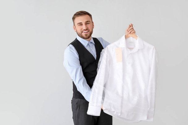 Male worker of modern dry-cleaner's with clothes on light background - Photo, image