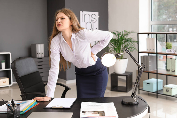Young businesswoman suffering from back pain in office - Фото, изображение