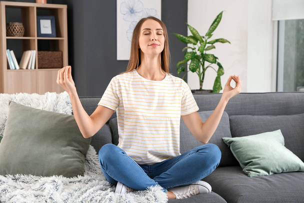 Beautiful young woman meditating at home - Foto, afbeelding