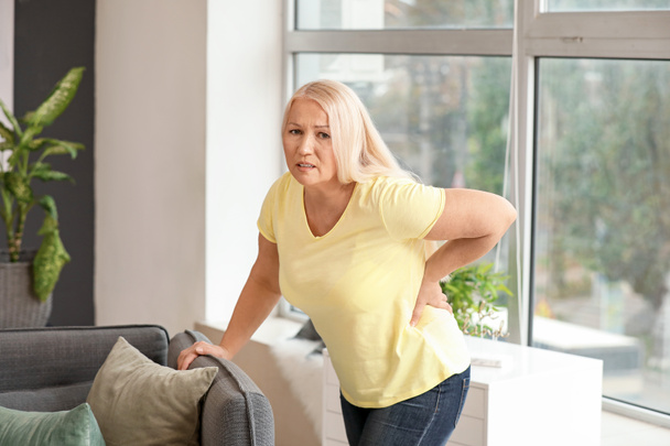 Зрелая женщина страдает от болей в спине дома
 - Фото, изображение