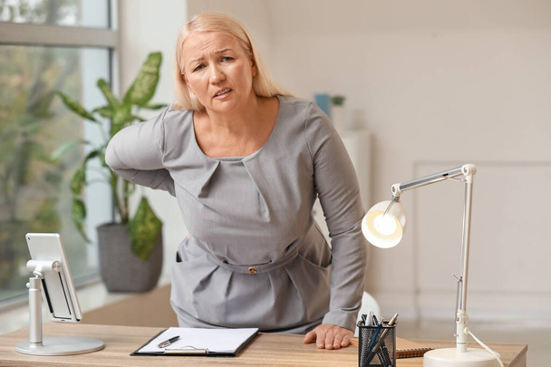 Mature woman suffering from back pain in office - Photo, Image