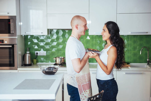 Beautiful young couple photographed smiling at the camera while cooking in the kitchen at home - Zdjęcie, obraz