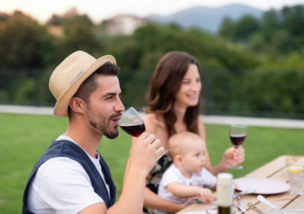 Young couple with baby sitting at table outdoors on family garden barbecue. - Foto, imagen