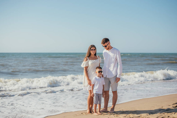šťastná mladá rodina s jedním dítětem stojí spolu na písečné pláži v létě - Fotografie, Obrázek