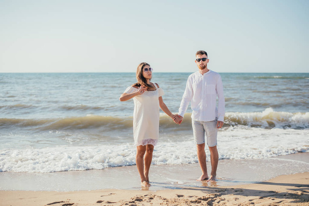 happy young couple holding hands and standing together on sandy beach  - Zdjęcie, obraz