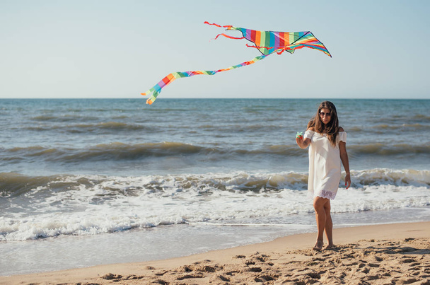 aantrekkelijke jonge vrouw met kleurrijke vlieger en wandelen op zandstrand - Foto, afbeelding