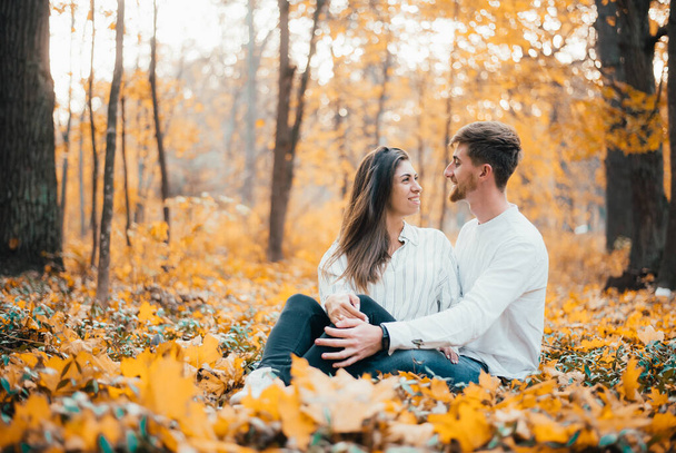 cheerful young couple sitting and hugging in autumn forest - Foto, afbeelding