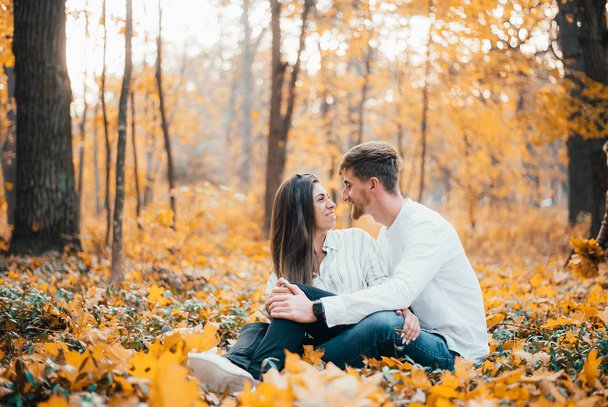 cheerful young couple sitting and hugging in autumn forest - Photo, image