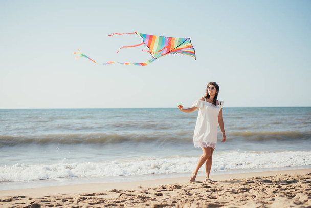 カラフルな凧を持って砂浜を歩く美しい幸せな若い女性 - 写真・画像