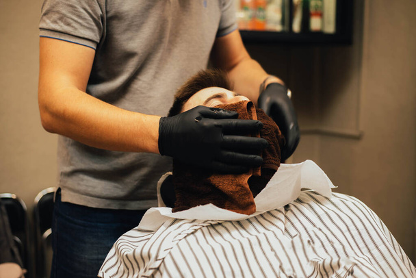Cropped closeup of a young man having his beard shaped in a barbershop  - Foto, imagen