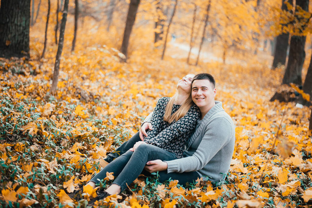 beautiful happy young couple sitting together on orange leaves in autumn forest - Foto, imagen