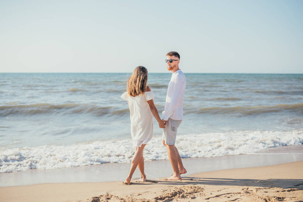 happy young couple holding hands together on sandy beach at summertime - Фото, изображение