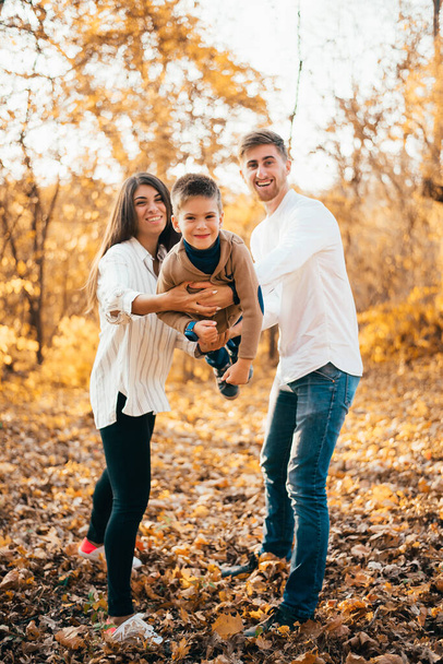 szczęśliwy młody rodzice i uroczy mały syn zabawy razem w jesiennym parku - Zdjęcie, obraz