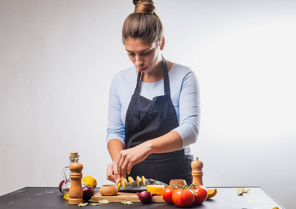 attractive young woman in apron preparing delicious fish with vegetables - Foto, afbeelding