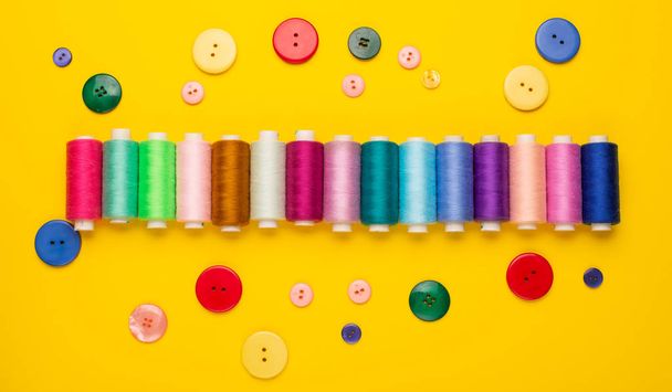 top view of colorful sewing threads and buttons on yellow background - Foto, Imagem