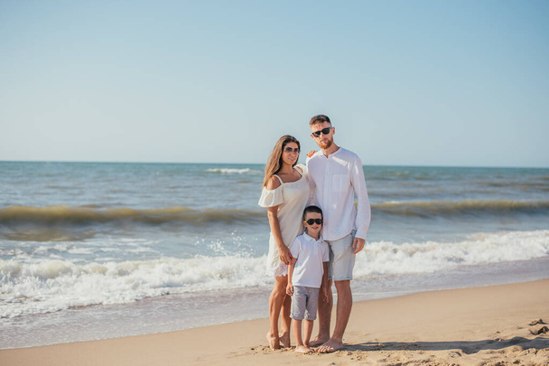 feliz jovem família com uma criança de pé juntos na praia de areia no verão
 - Foto, Imagem