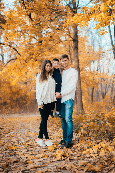 beautiful happy young family with one child smiling at camera in autumn park - Фото, изображение