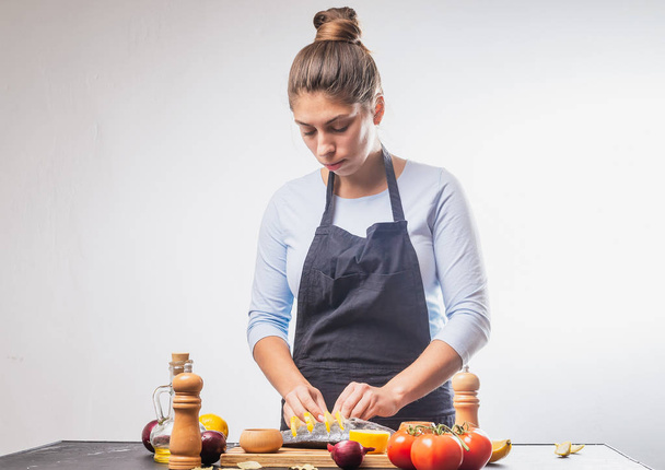 attractive young woman in apron preparing delicious fish with vegetables - Φωτογραφία, εικόνα
