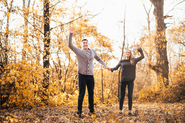 beautiful happy young couple holding hands and jumping in autumn park - Fotó, kép