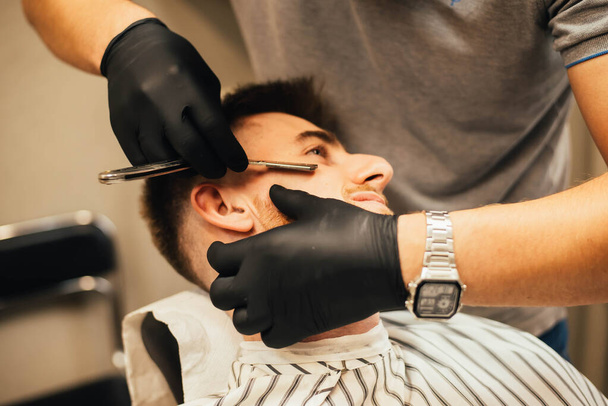 close-up partial view of barber shaving beard to man in barbershop - 写真・画像