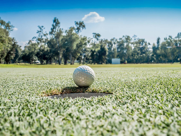 Foto van witte golfbal op gras met blauwe lucht achtergrond - Foto, afbeelding