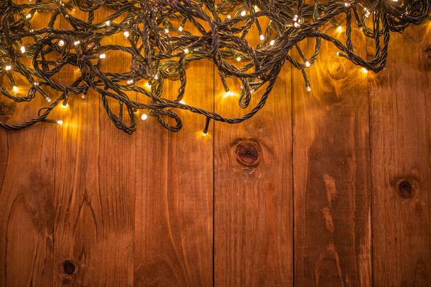 festive christmas background with illuminated garland on brown wooden background  - 写真・画像