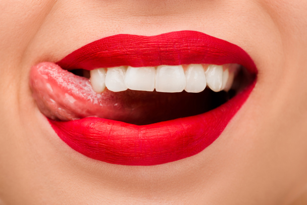 przycięty widok wesołej kobiety z czerwoną szminką wystający język izolowany na białym  - Zdjęcie, obraz