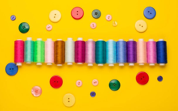 top view of colorful sewing threads and buttons on yellow background - Foto, afbeelding