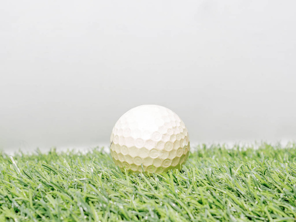 Zdjęcie żółtej piłki golfowej na sztucznej trawie z białym tłem - Zdjęcie, obraz