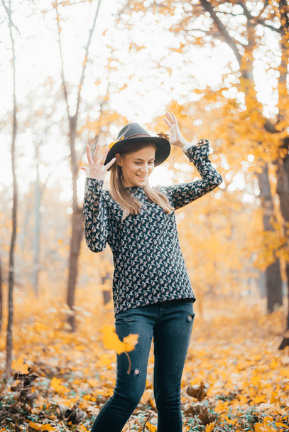 attractive young woman in hat standing in autumn forest - Fotografie, Obrázek