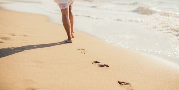 αποκομμένη φωτογραφία της νεαρής ξυπόλητης γυναίκας να περπατά στην αμμώδη παραλία - Φωτογραφία, εικόνα