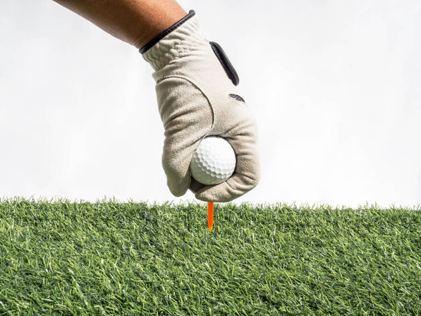 Bir el fotoğrafı. Golf topunu suni çimenli ve beyaz arka planlı bir tişörte yerleştiren bir el. - Fotoğraf, Görsel