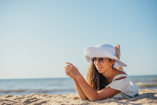 atraente sorrindo jovem mulher em chapéu e óculos de sol deitado na praia de areia no verão
 - Foto, Imagem