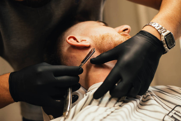 partial view of barber shaving beard to man in barbershop - Foto, immagini
