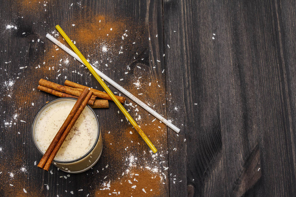 Traditional winter eggnog with milk, rum and cinnamon, sprinkle with grated nutmeg. Cocktail straws, dark wooden background - Foto, afbeelding