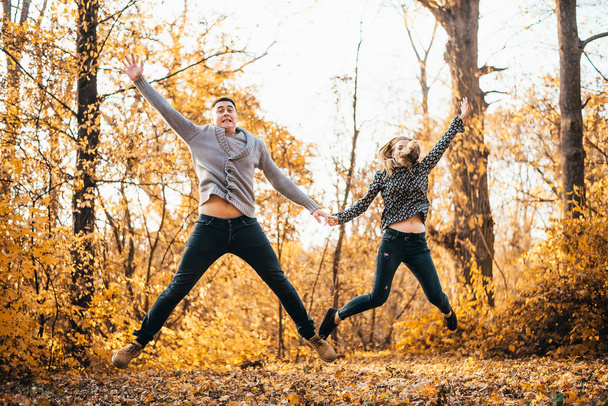 beautiful happy young couple holding hands and jumping in autumn park - Foto, afbeelding