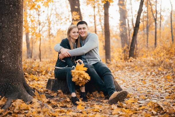 beautiful happy young couple sitting together and hugging in autumn forest - 写真・画像