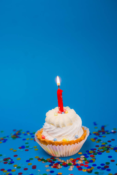 近くで見るおいしいお祝いのカップケーキ燃えるキャンドルと青の背景にカラフルなコンフェッティ - 写真・画像
