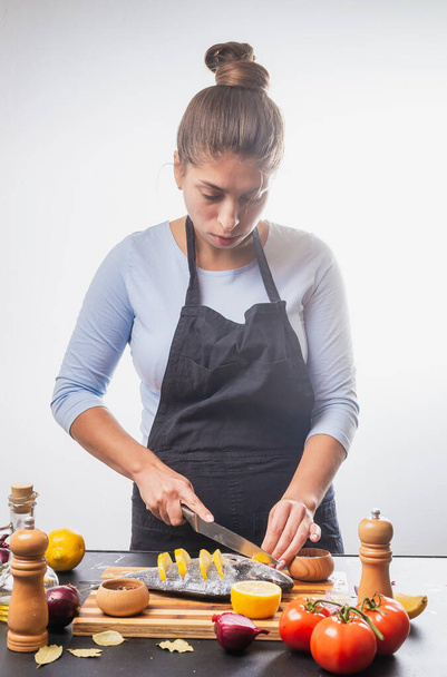 attractive young woman in apron preparing delicious fish with vegetables - Фото, изображение