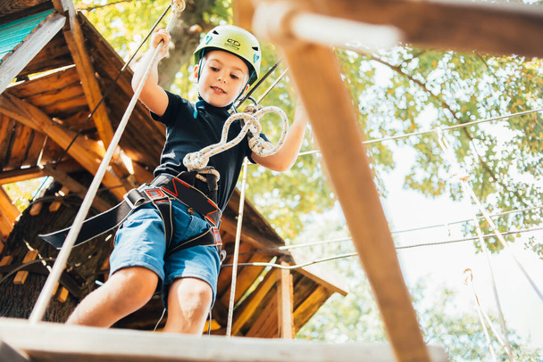 lage hoek uitzicht van schattige jongen genieten van activiteit in een klimmen avonturenpark op een zomer zonnige dag - Foto, afbeelding