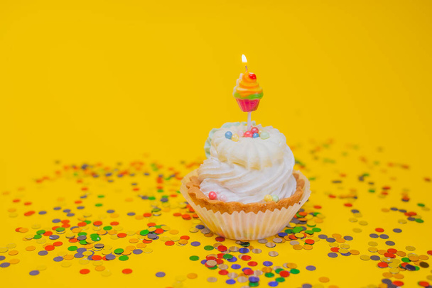 close-up uitzicht op heerlijke feestelijke cupcake met brandende kaars en kleurrijke confetti op gele achtergrond  - Foto, afbeelding