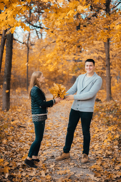 beautiful happy young couple holding orange leaves in autumn park - Foto, Imagen
