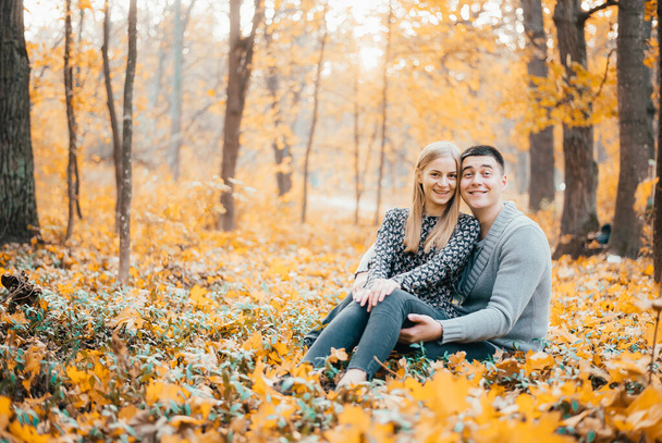 beautiful happy young couple sitting together on orange leaves in autumn forest - 写真・画像
