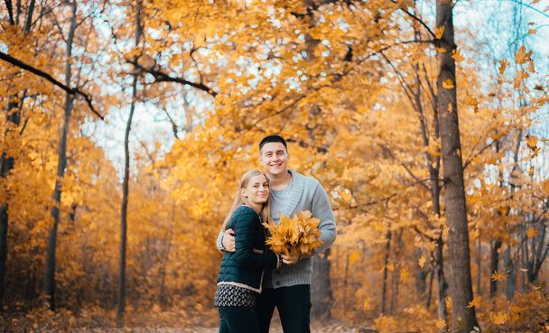beautiful happy young couple holding orange leaves in autumn park - Photo, image