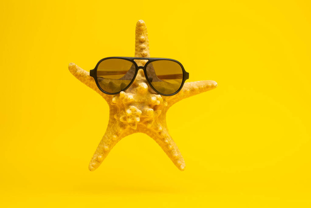 close-up view of starfish in sunglasses on yellow background, vacation concept - Fotó, kép
