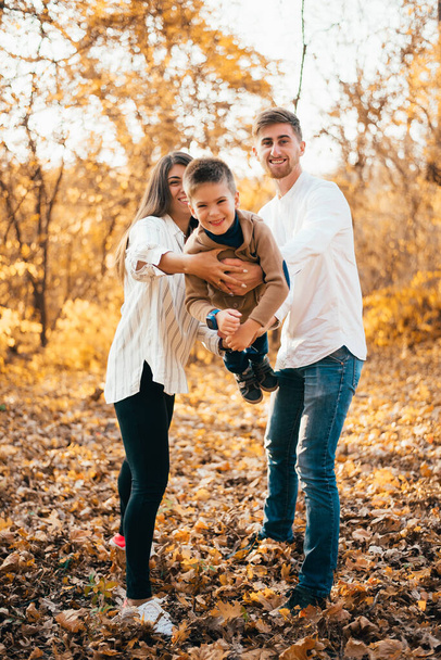 улыбающиеся молодые родители и милый маленький сын веселятся вместе в осеннем парке
 - Фото, изображение