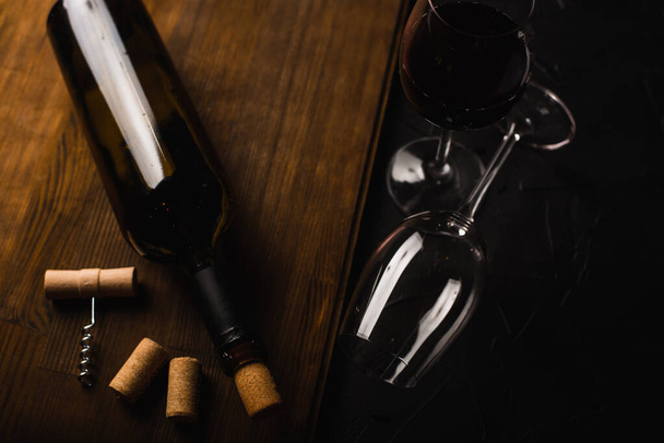 close-up zicht op wijnfles, glazen en kurkentrekker met kurken op zwart oppervlak - Foto, afbeelding