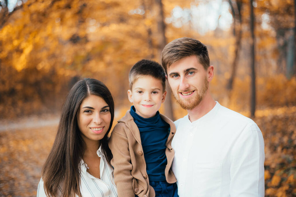 schöne glückliche junge Familie mit einem Kind, das im Herbstpark in die Kamera lächelt - Foto, Bild