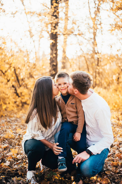 Ευτυχισμένη οικογένεια με ένα παιδί να περνάει χρόνο μαζί στο πάρκο το φθινόπωρο. - Φωτογραφία, εικόνα