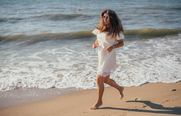 beautiful young woman running on sandy beach near sea at sunny summer day - Foto, Imagen